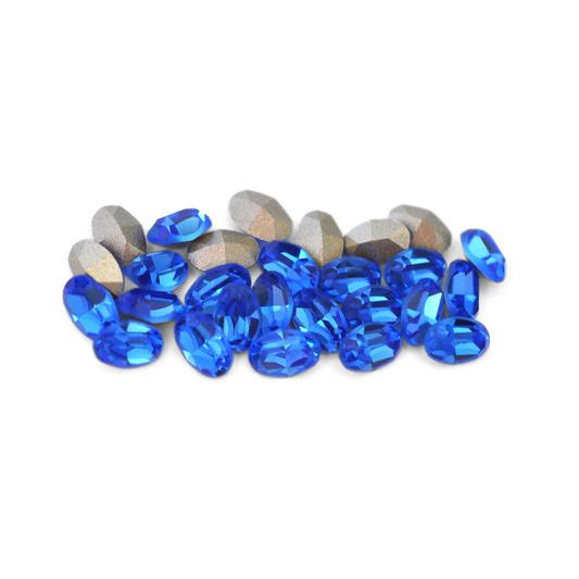 Oval shaped faceted Austrian crystal rhinestones in the color Sapphire displayed on a white background.
