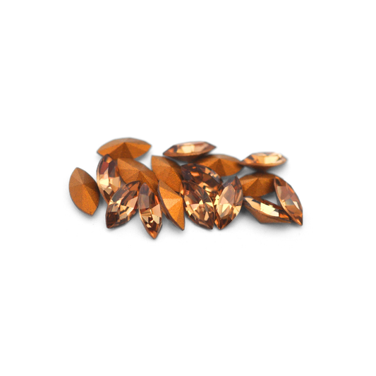 Navette shaped faceted Austrian crystal rhinestones in the color Light Colorado Topaz displayed on a white background.