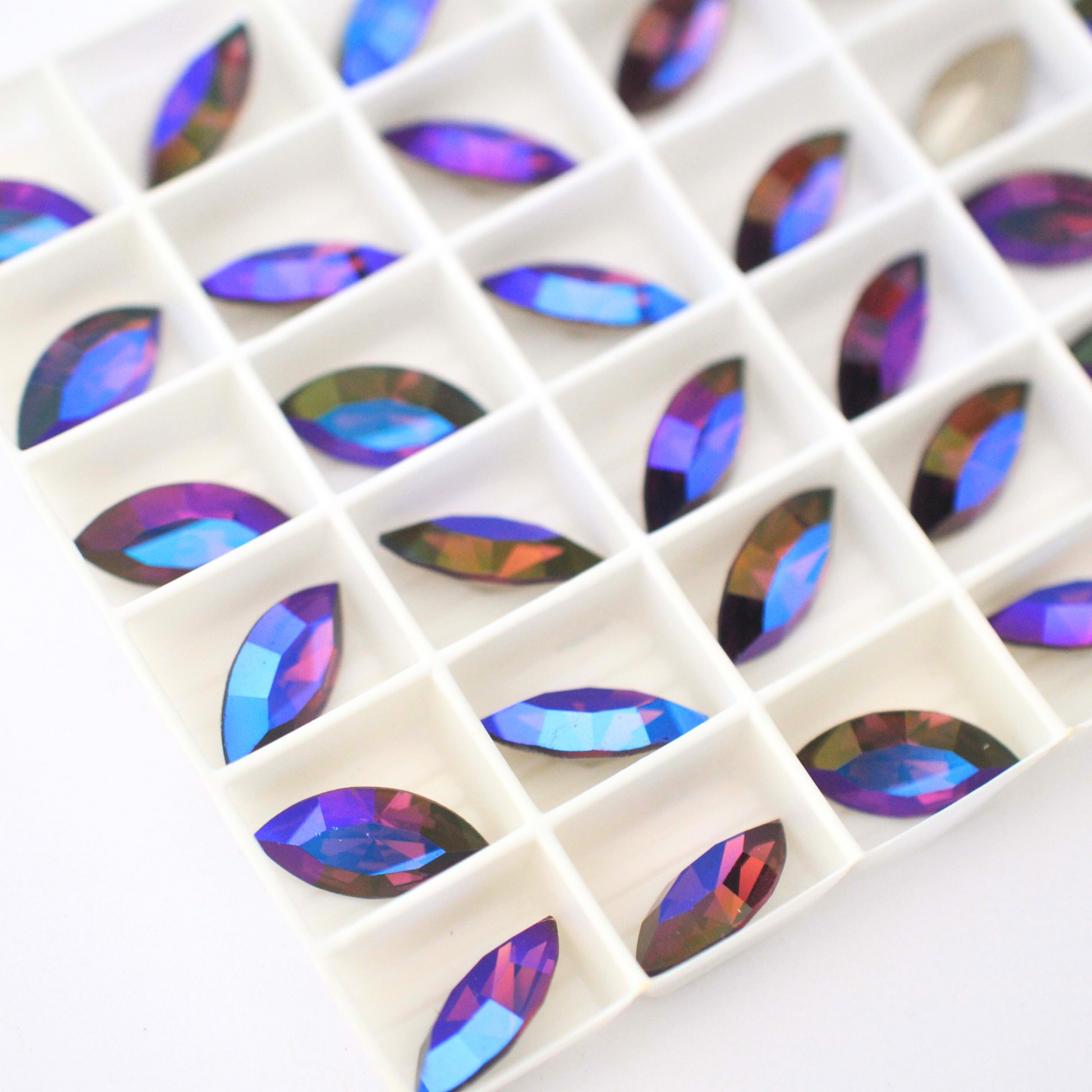 Navette shaped faceted Austrian crystal rhinestones in the color Amethyst Glacier Blue displayed in a tray on a white background.