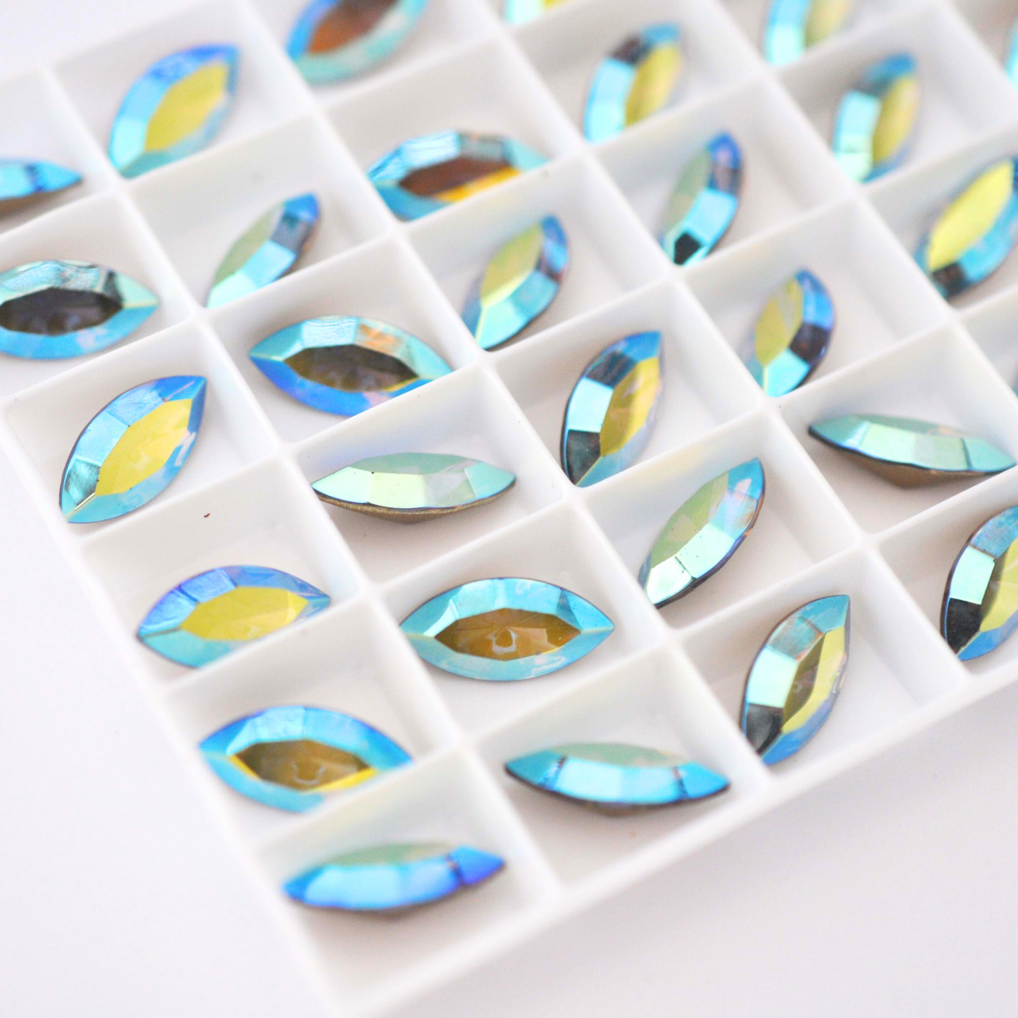Navette shaped faceted Austrian crystal rhinestones in the color Light Colorado Topaz AB displayed in a tray on a white background.