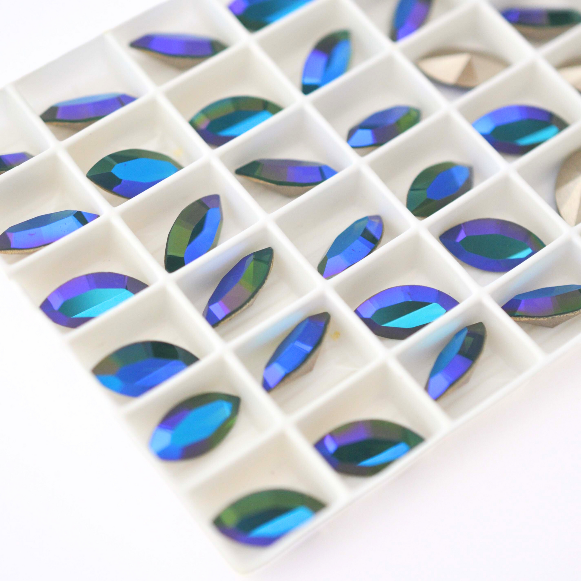 Navette shaped faceted Austrian crystal rhinestones in the color Palace Green Opal Glacier Blue displayed in a tray on a white background.