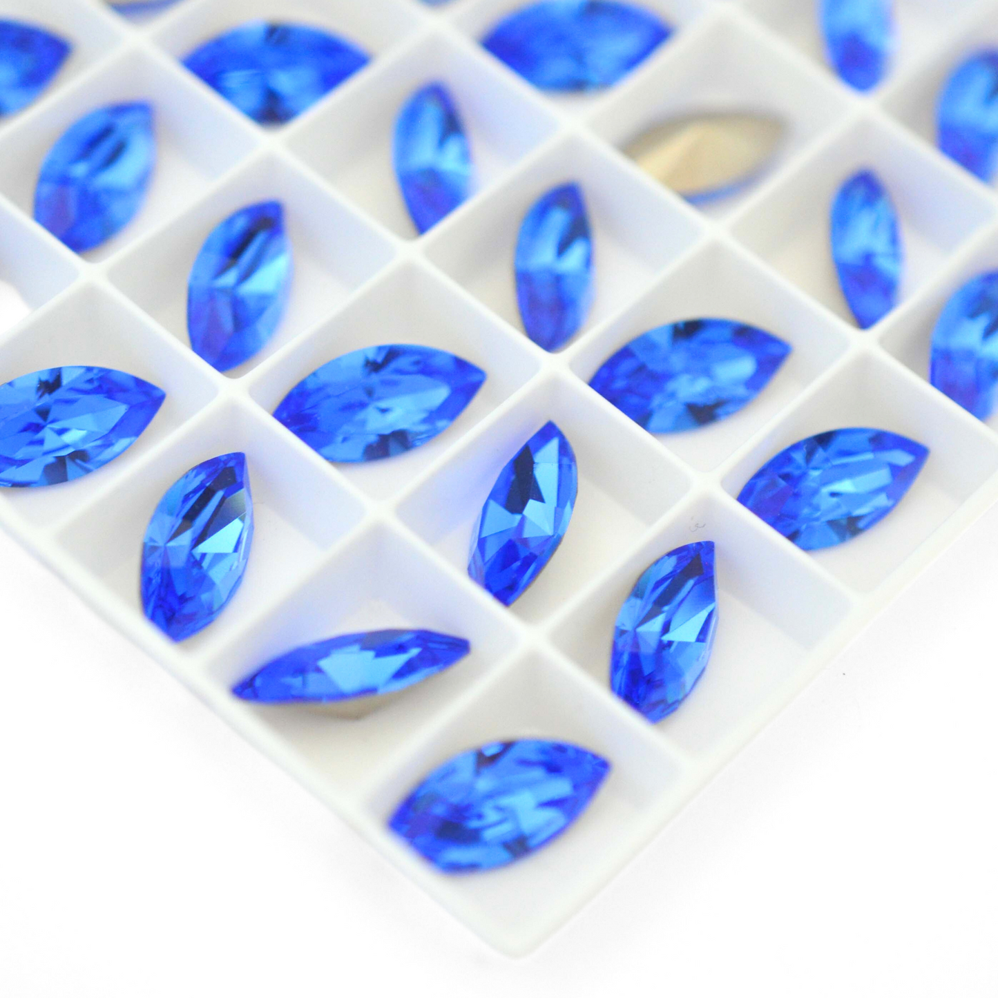 Navette shaped faceted Austrian crystal rhinestones in the color Sapphire displayed on a white background.