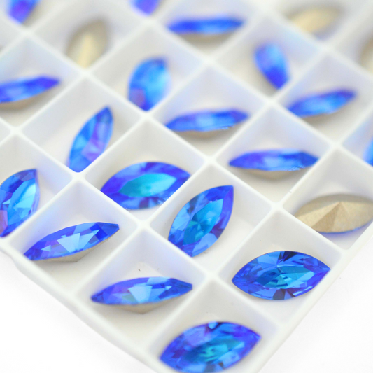 Navette shaped faceted Austrian crystal rhinestones in the color Sapphire Glacier Blue displayed on a white background.