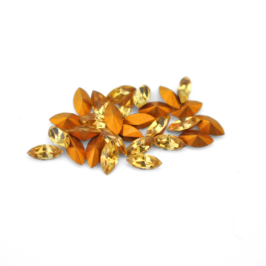 Navette shaped faceted Austrian crystal rhinestones in the color Light Topaz displayed on a white background.