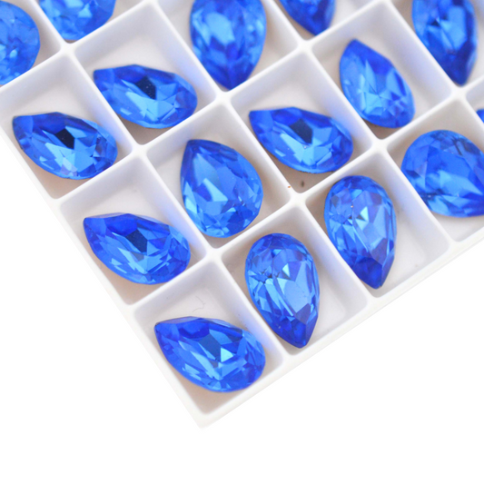Pear shape faceted Austrian crystal rhinestones in the color Sapphire displayed on a white background.