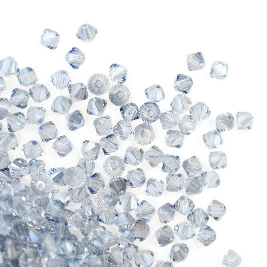 Austrian crystal 5328 bicone beads in the color Blue Shade spilling out onto a white background.