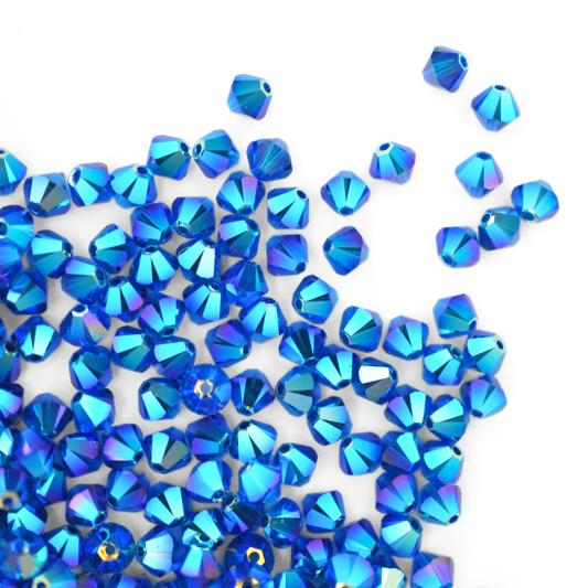 Austrian crystal 5328 bicone beads in the color Capri Blue AB 2X spilling out onto a white background.