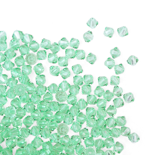 Austrian crystal 5328 bicone beads in the color Chrysolite spilling out onto a white background.