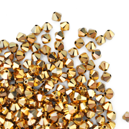 Austrian crystal 5328 bicone beads in the color Dorado 2X spilling out onto a white background.