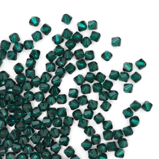 Austrian crystal 5328 bicone beads in the color Emerald spilling out onto a white background.