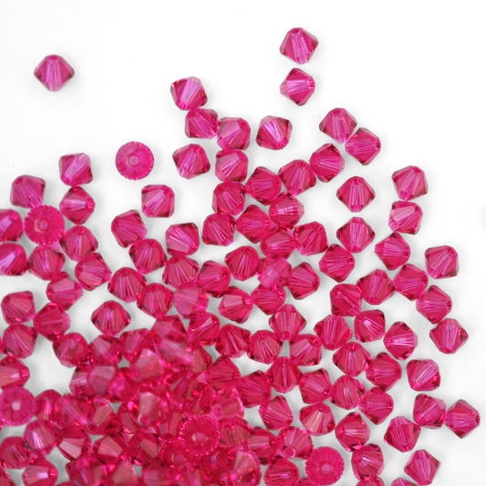 Austrian crystal 5328 bicone beads in the color Fuchsia spilling out onto a white background.