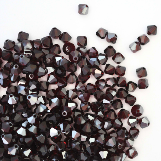 Austrian crystal 5328 bicone beads in the color Garnet Satin spilling out onto a white background.