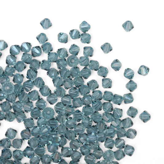 Austrian crystal 5328 bicone beads in the color Indian Sapphire spilling out onto a white background.