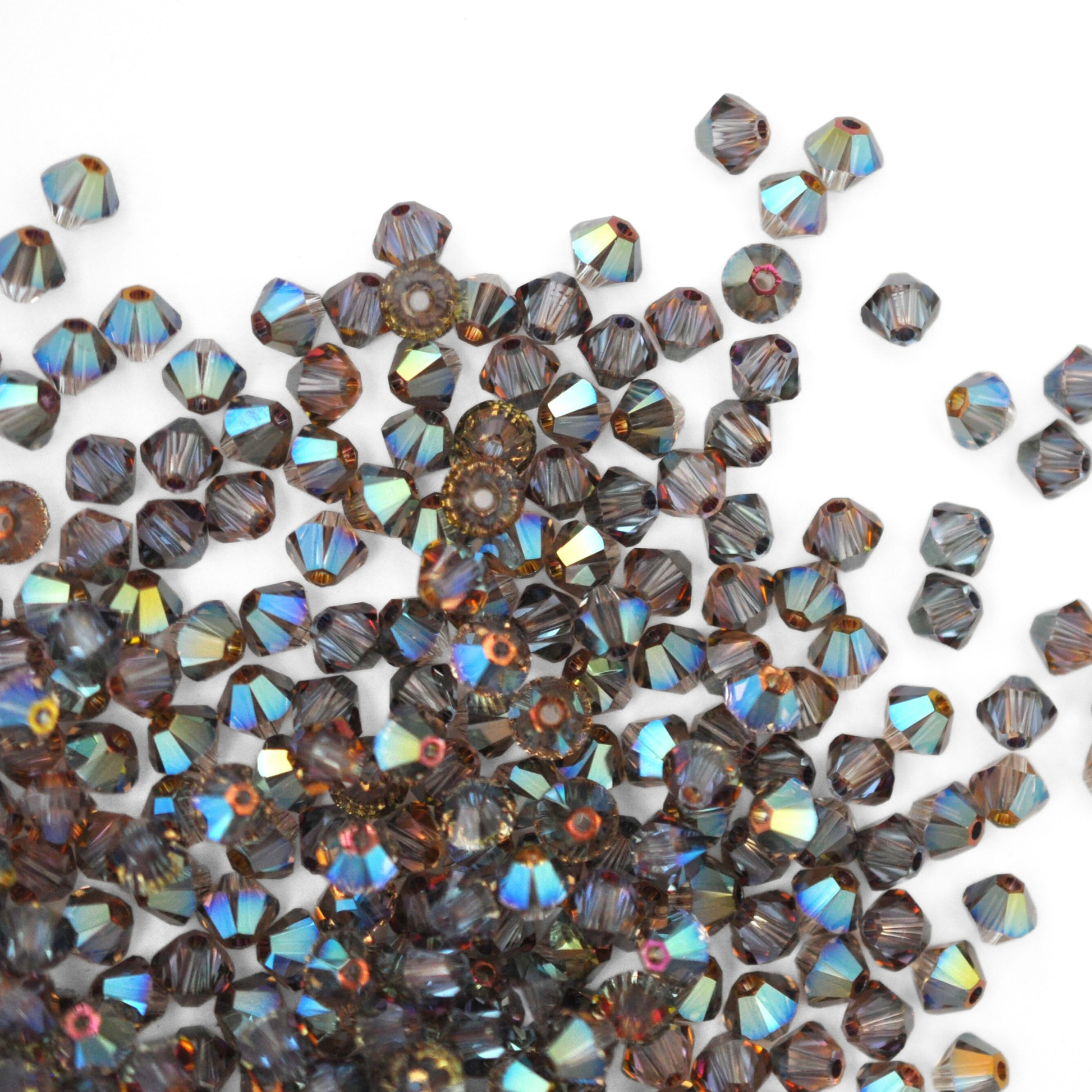 Austrian crystal 5328 bicone beads in the color Iridescent Green spilling out onto a white background.