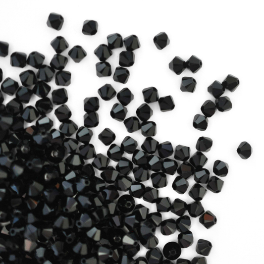 Austrian crystal 5328 bicone beads in the color Jet spilling out onto a white background.