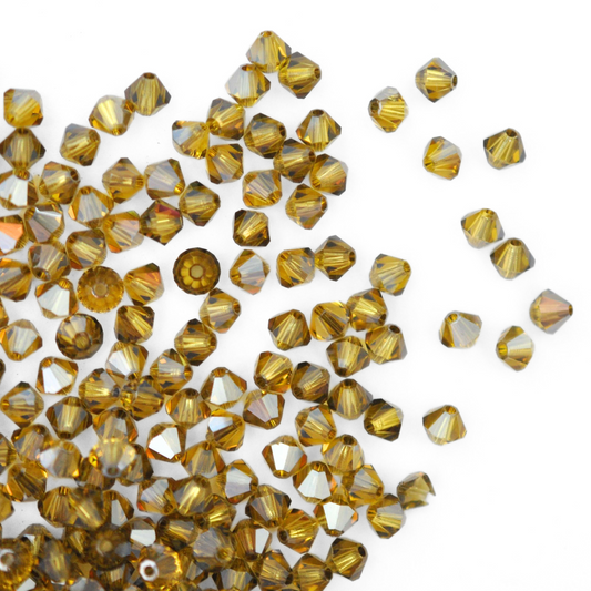 Austrian crystal 5328 bicone beads in the color Light Topaz Satin spilling out onto a white background.