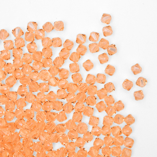 Austrian crystal 5328 bicone beads in the color Light Peach spilling out onto a white background.