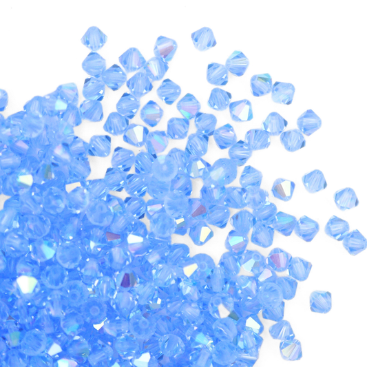 Austrian crystal 5328 bicone beads in the color Light Sapphire AB spilling out onto a white background.