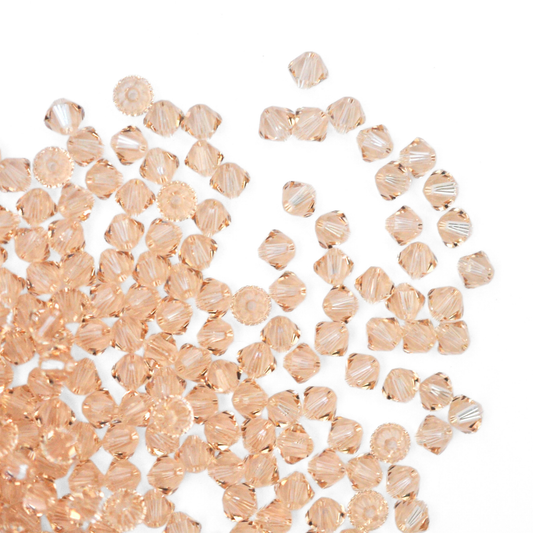 Austrian crystal 5328 bicone beads in the color Light Silk spilling out onto a white background.