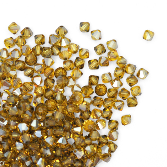 Austrian crystal 5328 bicone beads in the color Light Topaz Satin spilling out onto a white background.