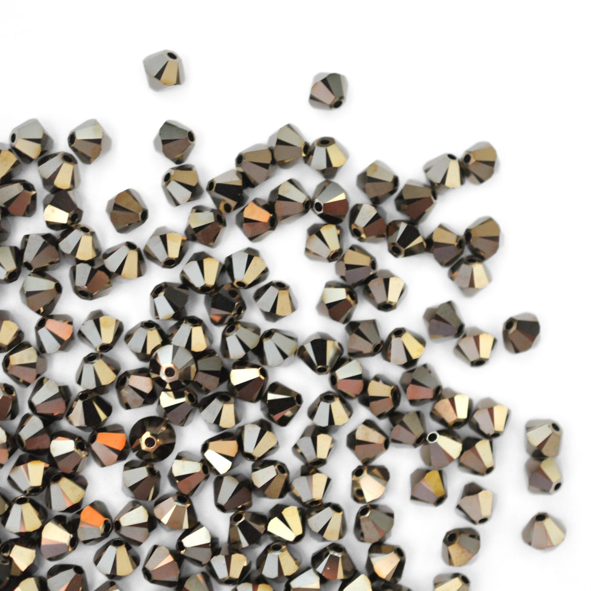 Austrian crystal 5328 bicone beads in the color Metallic Light Gold 2X spilling out onto a white background.