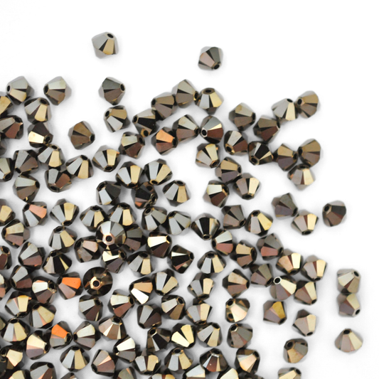 Austrian crystal 5328 bicone beads in the color Metallic Light Gold 2X spilling out onto a white background.