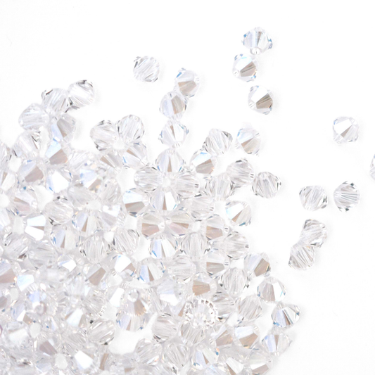 Austrian crystal 5328 bicone beads in the color Moonlight spilling out onto a white background.