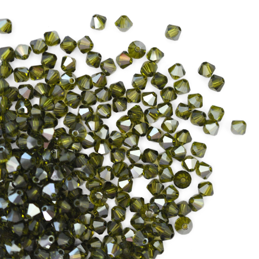 Austrian crystal 5328 bicone beads in the color Olivine Satin spilling out onto a white background.