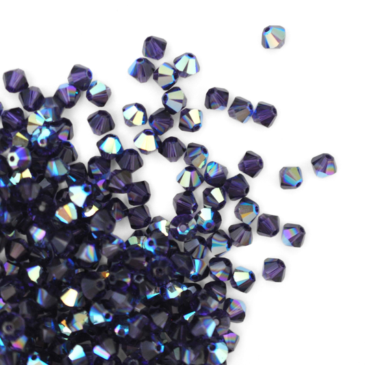 Austrian crystal 5328 bicone beads in the color Purple Velvet AB spilling out onto a white background.