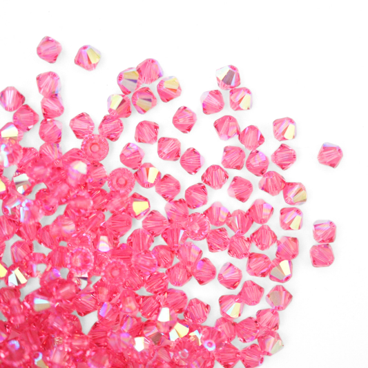 Austrian crystal 5328 bicone beads in the color Rose AB spilling out onto a white background.