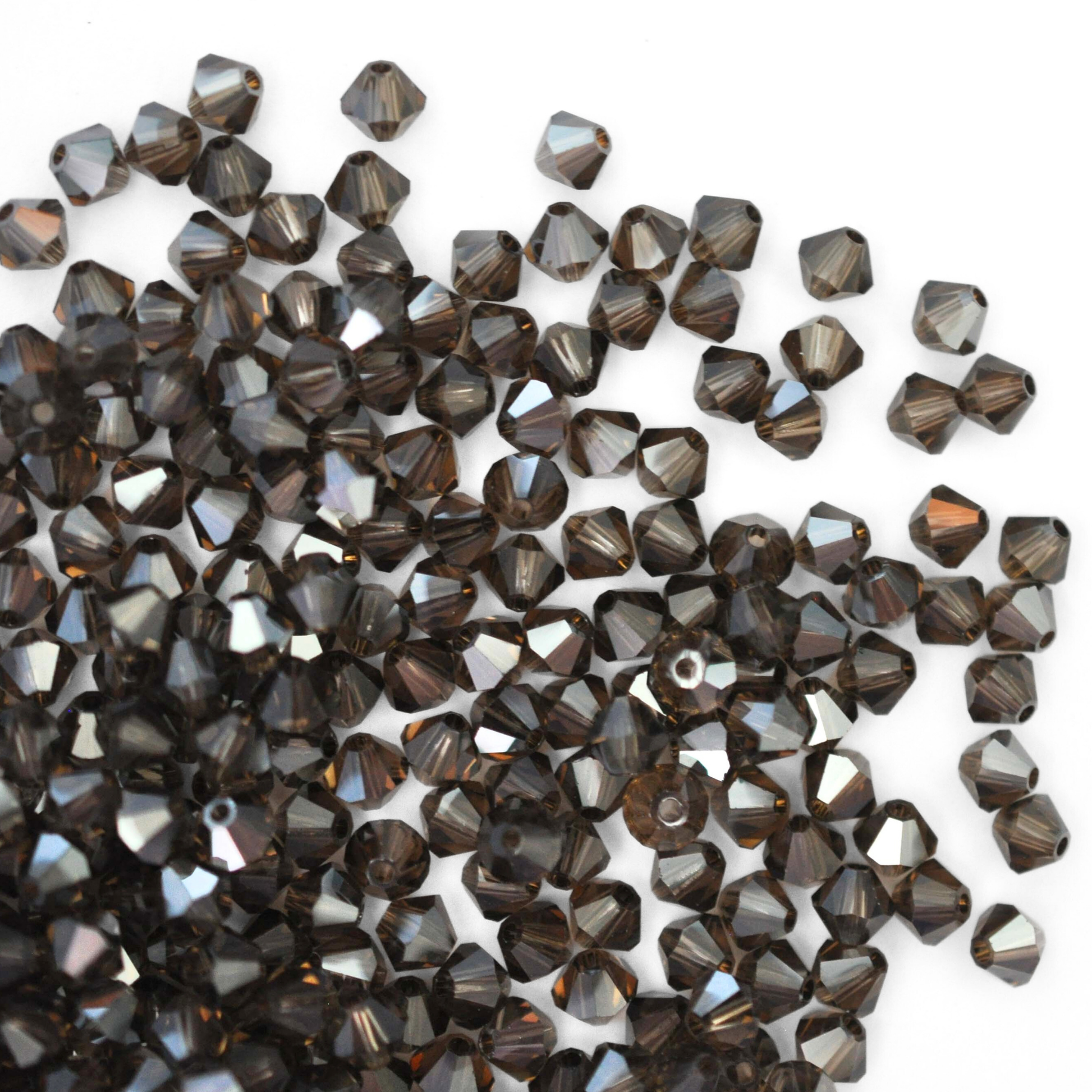 Austrian crystal 5328 bicone beads in the color Smoky Quartz Satin spilling out onto a white background.