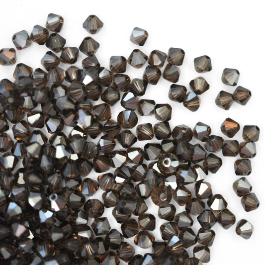 Austrian crystal 5328 bicone beads in the color Smoky Quartz Satin spilling out onto a white background.