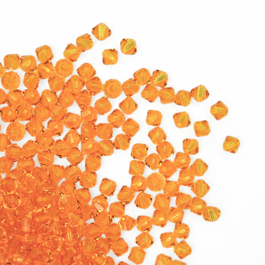 Austrian crystal 5328 bicone beads in the color Sunflower spilling out onto a white background.
