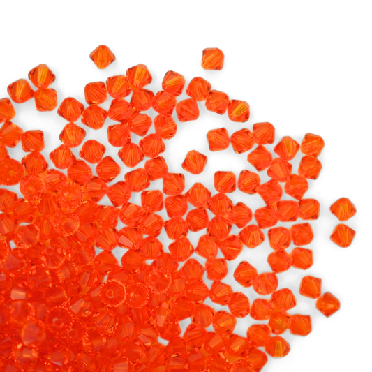 Austrian crystal 5328 bicone beads in the color Tangerine spilling out onto a white background.
