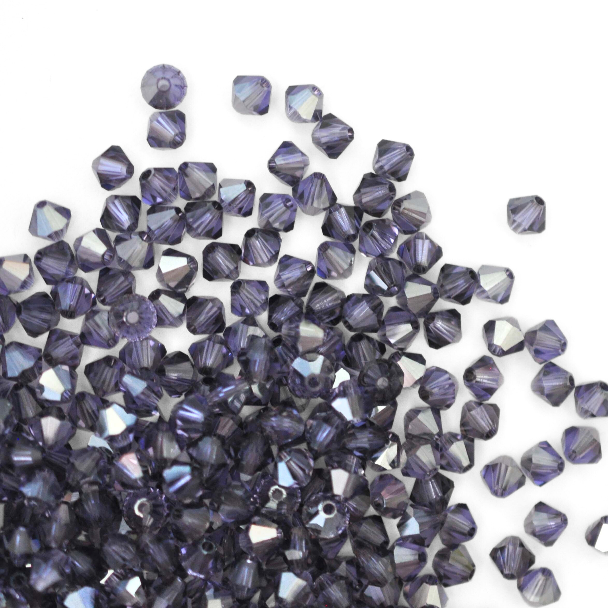 Austrian crystal 5328 bicone beads in the color Tanzanite Satin spilling out onto a white background.