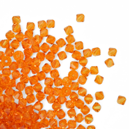 Austrian crystal 5328 bicone beads in the color Topaz spilling out onto a white background.