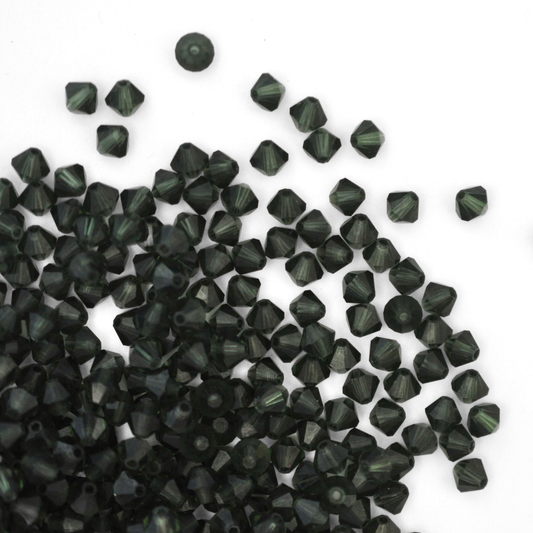 Austrian crystal 5328 bicone beads in the color Turmaline spilling out onto a white background.