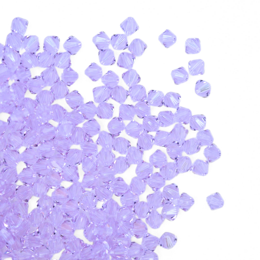 Austrian crystal 5328 bicone beads in the color Violet spilling out onto a white background.