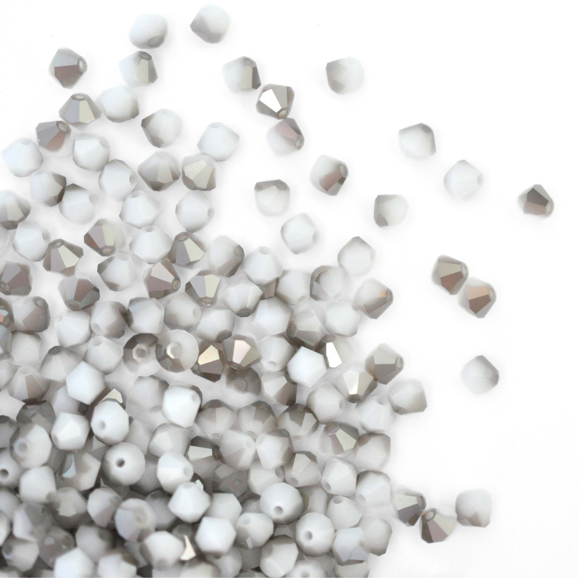 Austrian crystal 5328 bicone beads in the color White Alabaster Satin spilling out onto a white background.