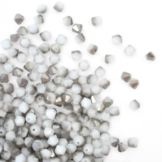 Austrian crystal 5328 bicone beads in the color White Alabaster Satin spilling out onto a white background.