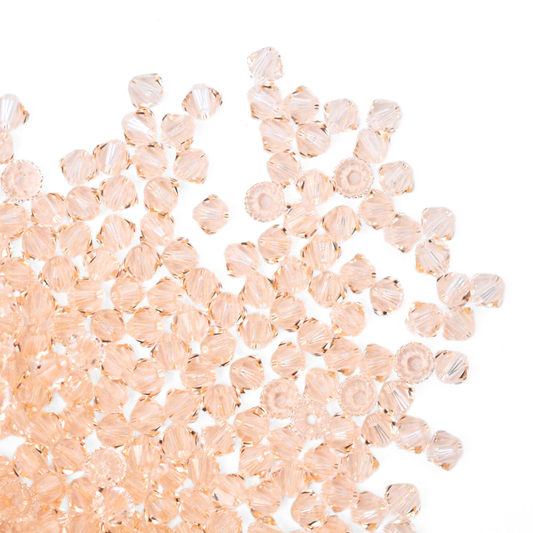 Austrian crystal 5328 bicone beads in the color Silk spilling out onto a white background.