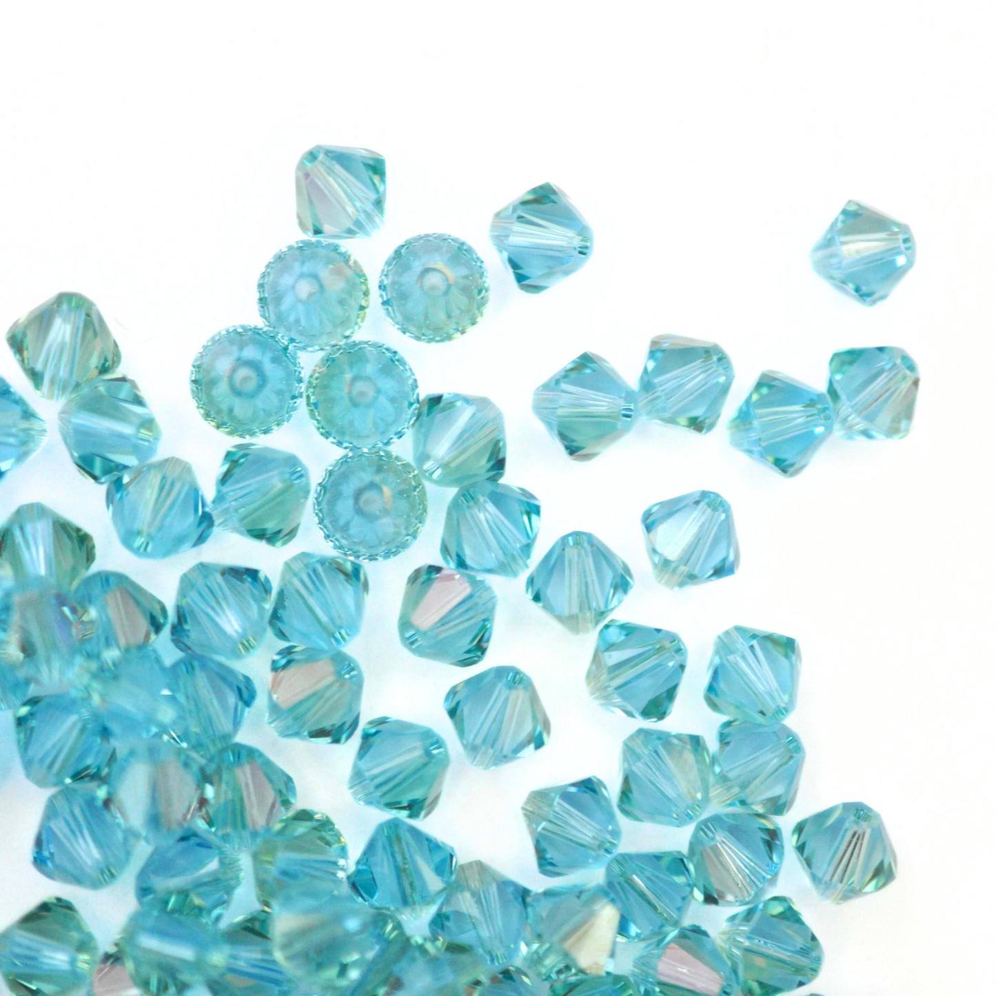 Austrian crystal 5328 bicone beads in the color Aquamarine Champagne spilling out onto a white background.