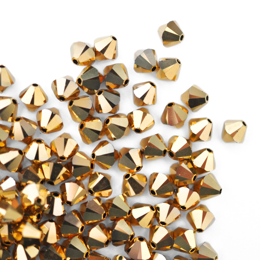 Austrian crystal 5328 bicone beads in the color Aurum 2X spilling out onto a white background.