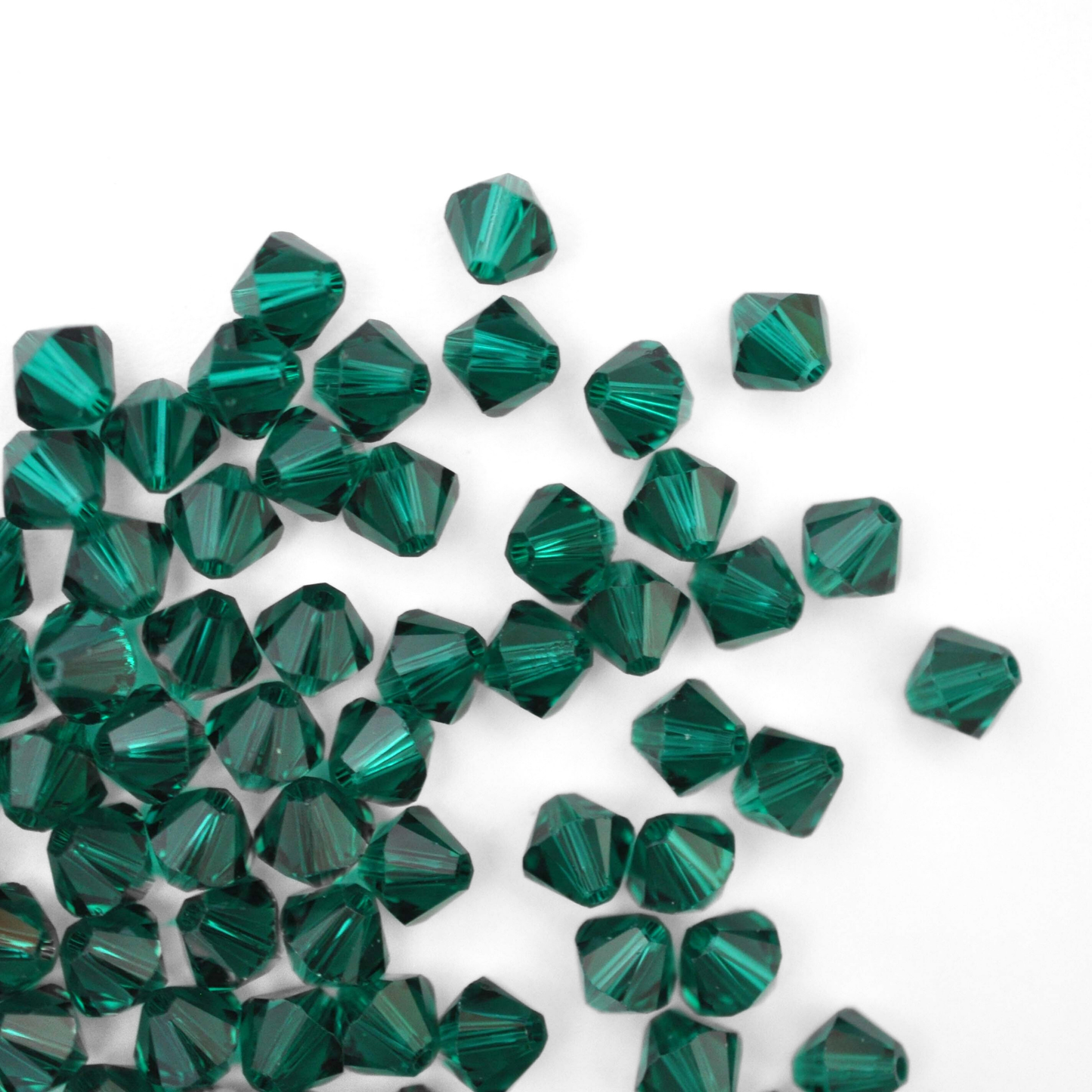 Austrian crystal 5328 bicone beads in the color Emerald spilling out onto a white background.