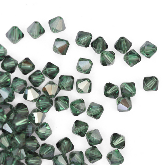 Austrian crystal 5328 bicone beads in the color Erinite Satin spilling out onto a white background.