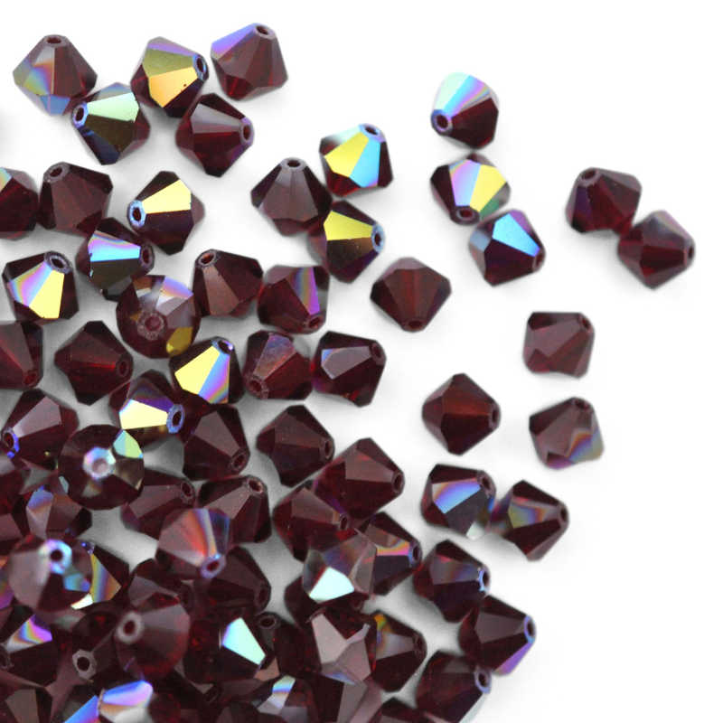 Austrian crystal 5328 bicone beads in the color Garnet AB spilling out onto a white background.