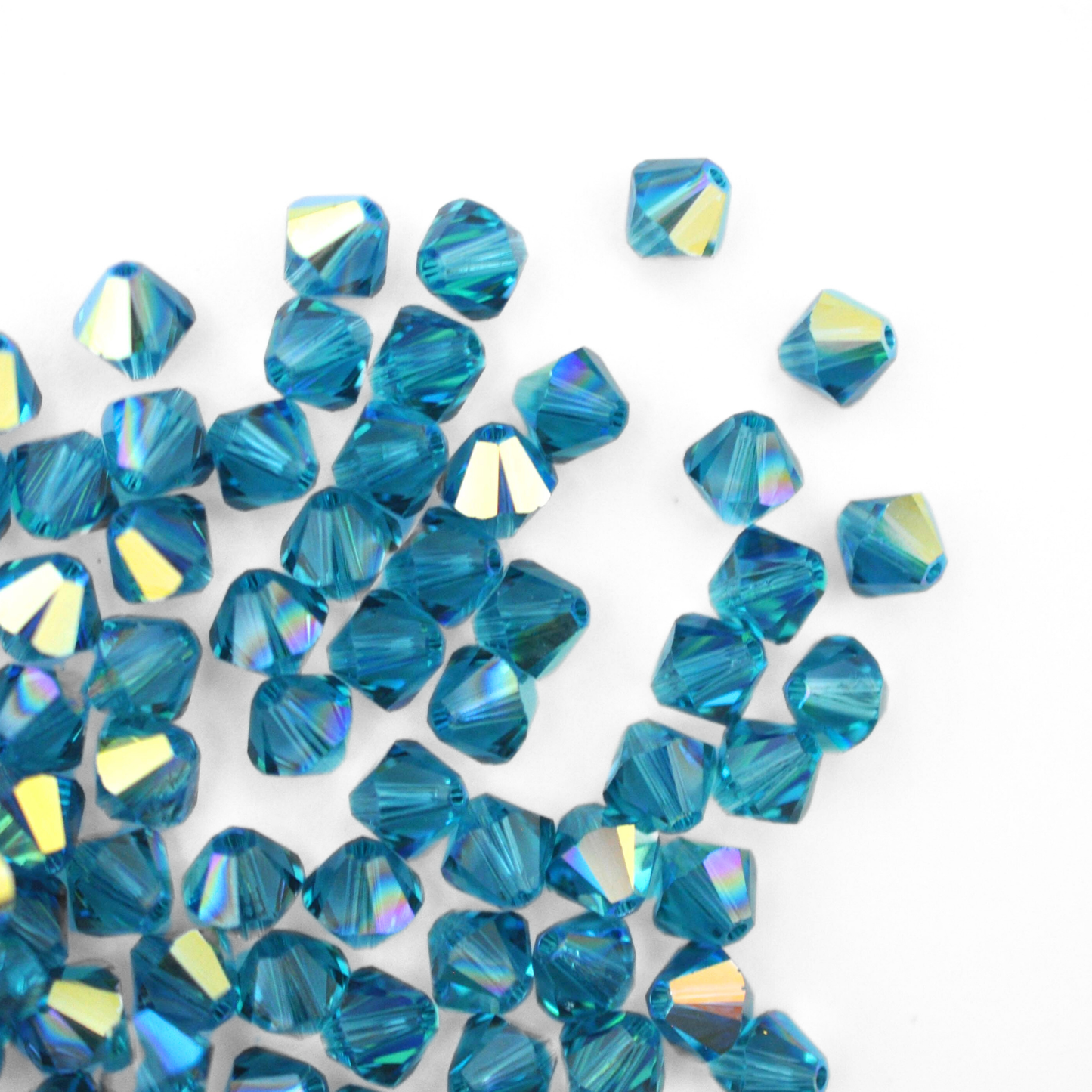 Austrian crystal 5328 bicone beads in the color Indicolite AB spilling out onto a white background.