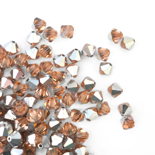 Austrian crystal 5328 bicone beads in the color Light Peach CAL spilling out onto a white background.