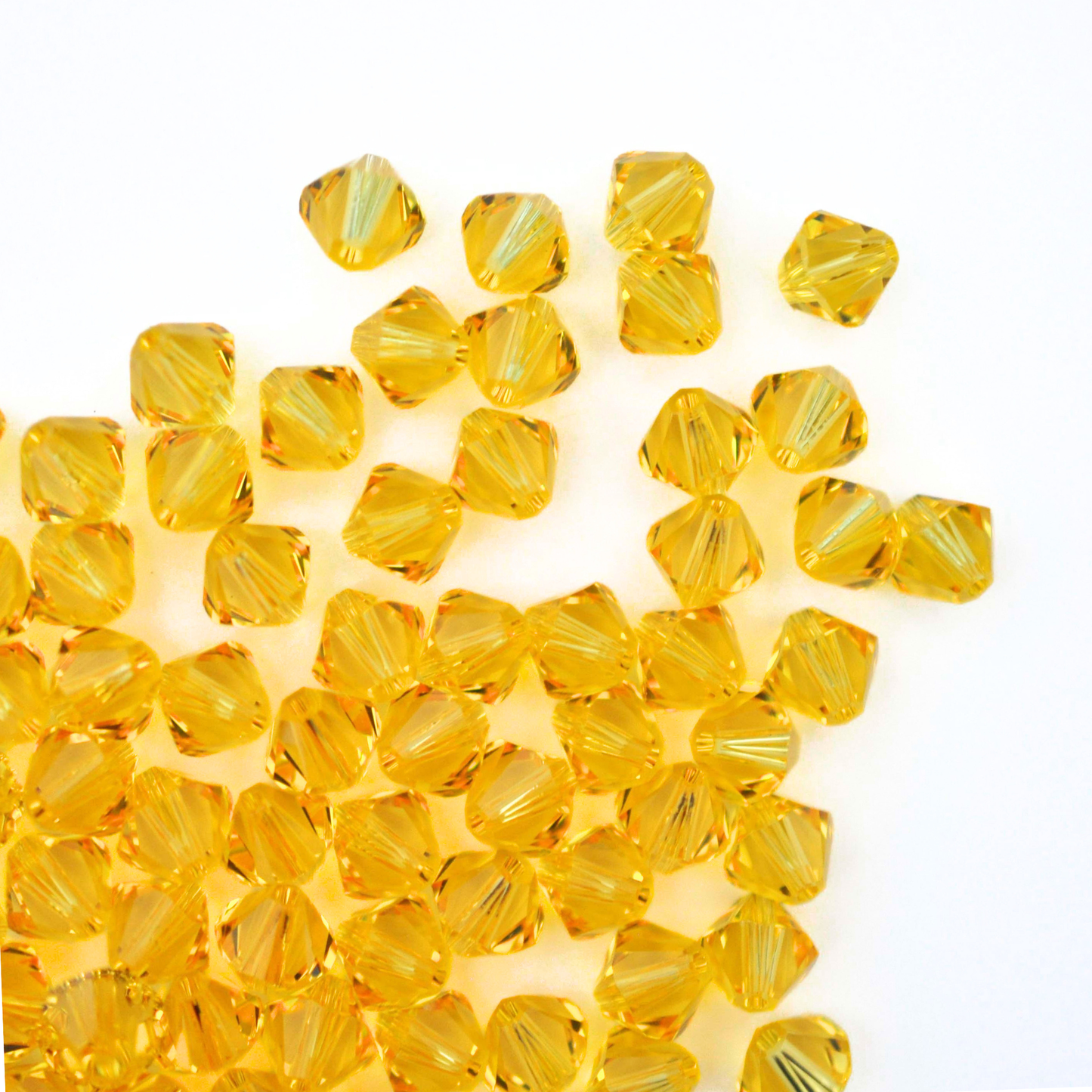Austrian crystal 5328 bicone beads in the color Light Topaz spilling out onto a white background.