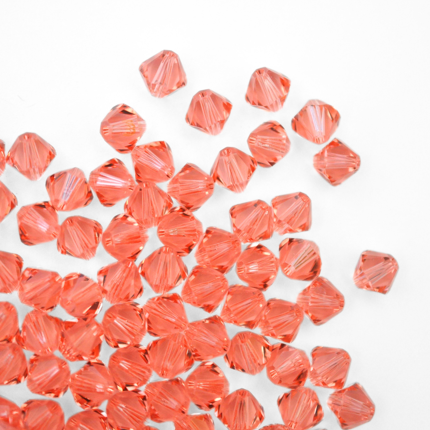 Austrian crystal 5328 bicone beads in the color Rose Peach spilling out onto a white background.